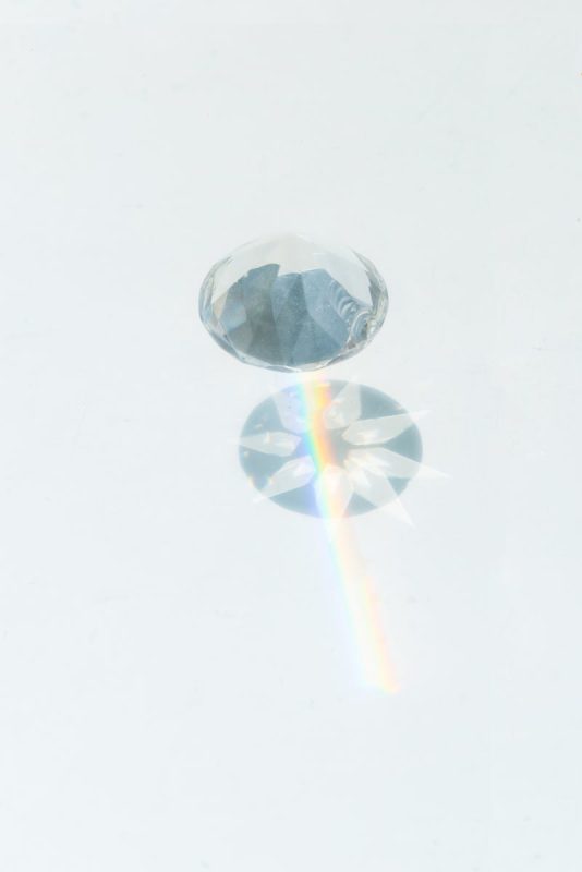 A sparkling diamond casting vibrant rainbow reflections on a smooth white background.
