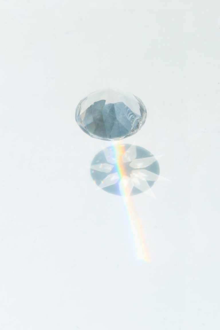 A sparkling diamond casting vibrant rainbow reflections on a smooth white background.